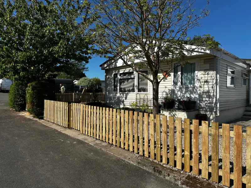 A house with a fence surrounding it, featuring a car parked in front on a clear day