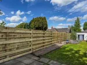 Modern horizontal timber slatted fence installed in a residential Midlothian garden with lawn, paving, and blue sky background.